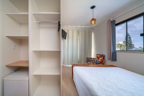 Quarto com cama, televisão, janela com cortinas e vista para o exterior.