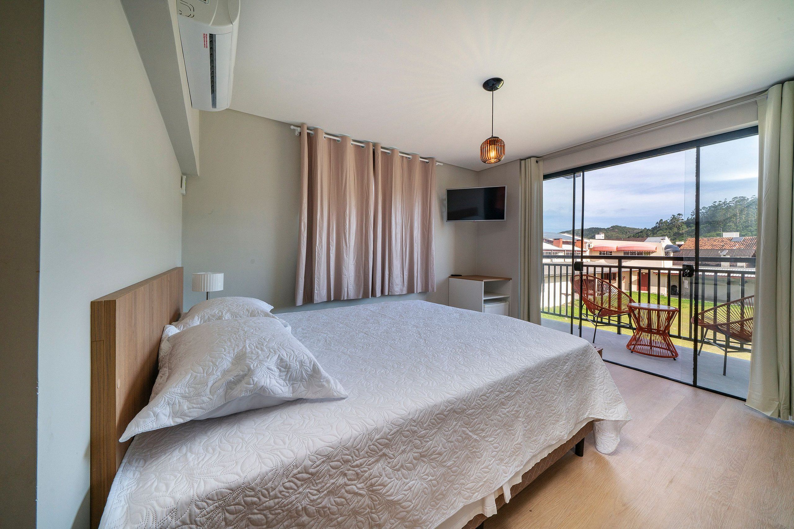 Un dormitorio con una cama grande, un televisor montado en la pared y un balcón con mobiliario exterior.