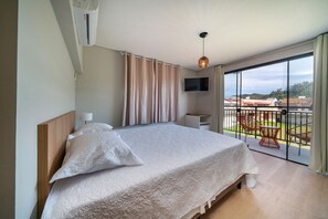 Een slaapkamer met een groot bed, een aan de muur bevestigde televisie en een balkon met buitenmeubilair.
