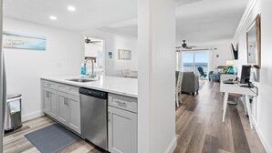 Una cocina moderna con electrodomésticos de acero inoxidable, un comedor con una silla gris y vista al océano a través de un ventanal grande.