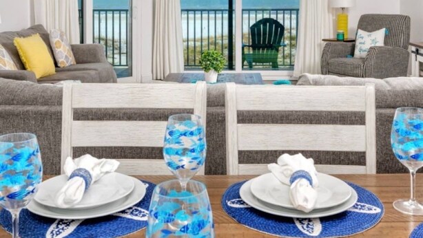 Un comedor con una mesa dispuesta para dos, vistas al océano a través de amplios ventanales y un balcón con una silla.
