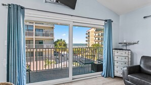 A balcony with a view of a building and palm trees, a black leather sofa, and a metal cabinet. - Stay Beachside I Stunning Views Walk Everywhere (Clearwater Beach)