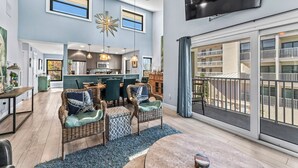 A spacious living room with a large TV, dining area, and kitchen. - Stay Beachside I Stunning Views Walk Everywhere (Clearwater Beach)
