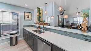 A modern kitchen with a large island, stainless steel appliances, pendant lighting, and a view to the dining area. - Stay Beachside I Stunning Views Walk Everywhere (Clearwater Beach)