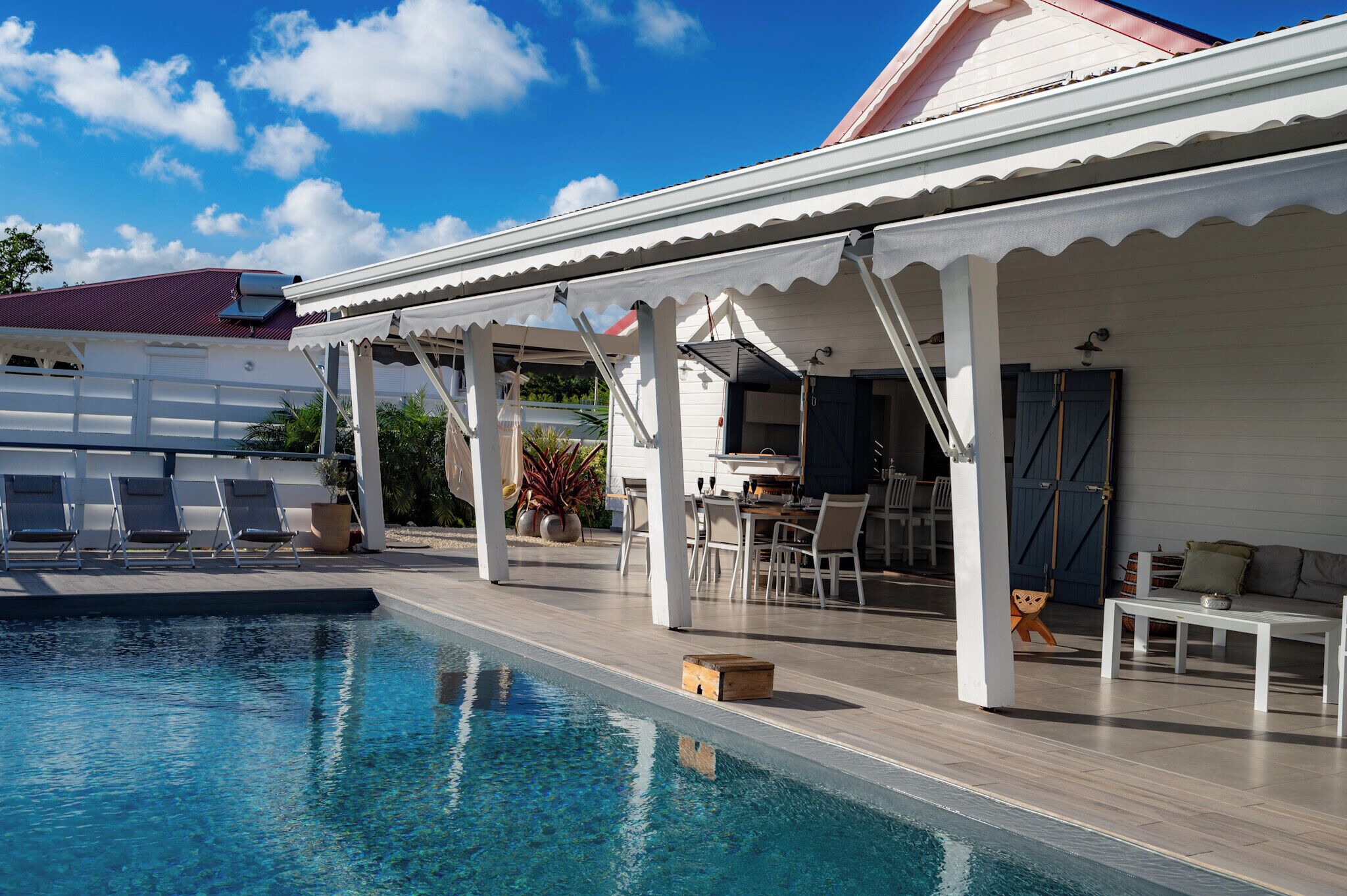 A poolside area with lounge chairs, a dining table, and a covered seating area.