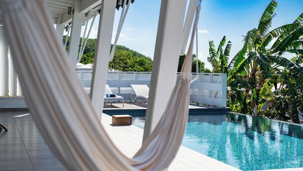 A hammock by a pool with lounge chairs and palm trees in the background. - Villa Paruline with swimming pool tropical garden and sea view (Grand-Bourg)