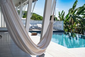 A hammock by a pool with lounge chairs and palm trees in the background.