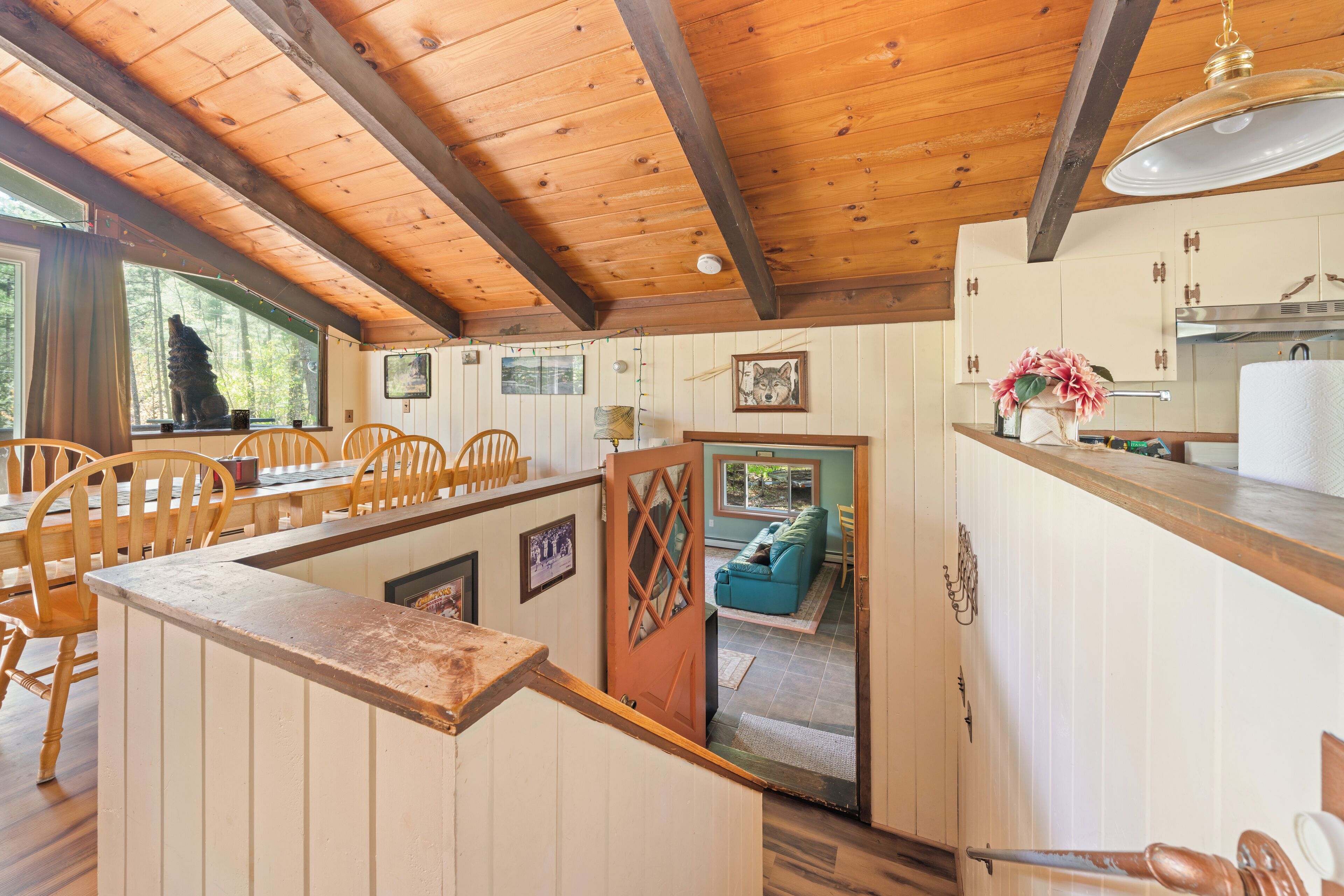 A rustic cabin interior with wooden beams, a dining area with chairs, a kitchen with cabinets, and a cozy living space with a couch.