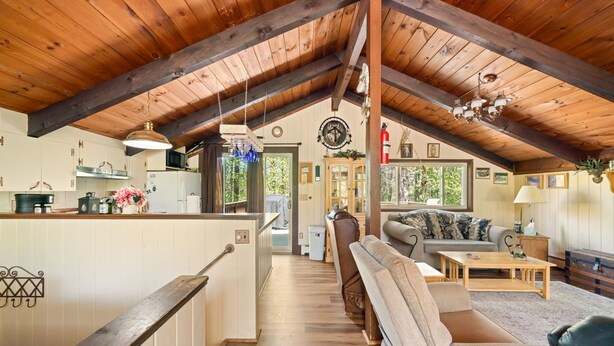 Un loft amplio con techo alto, vigas de madera, zona de cocina, sala de estar con sofá y mesa de centro, y vistas al exterior.