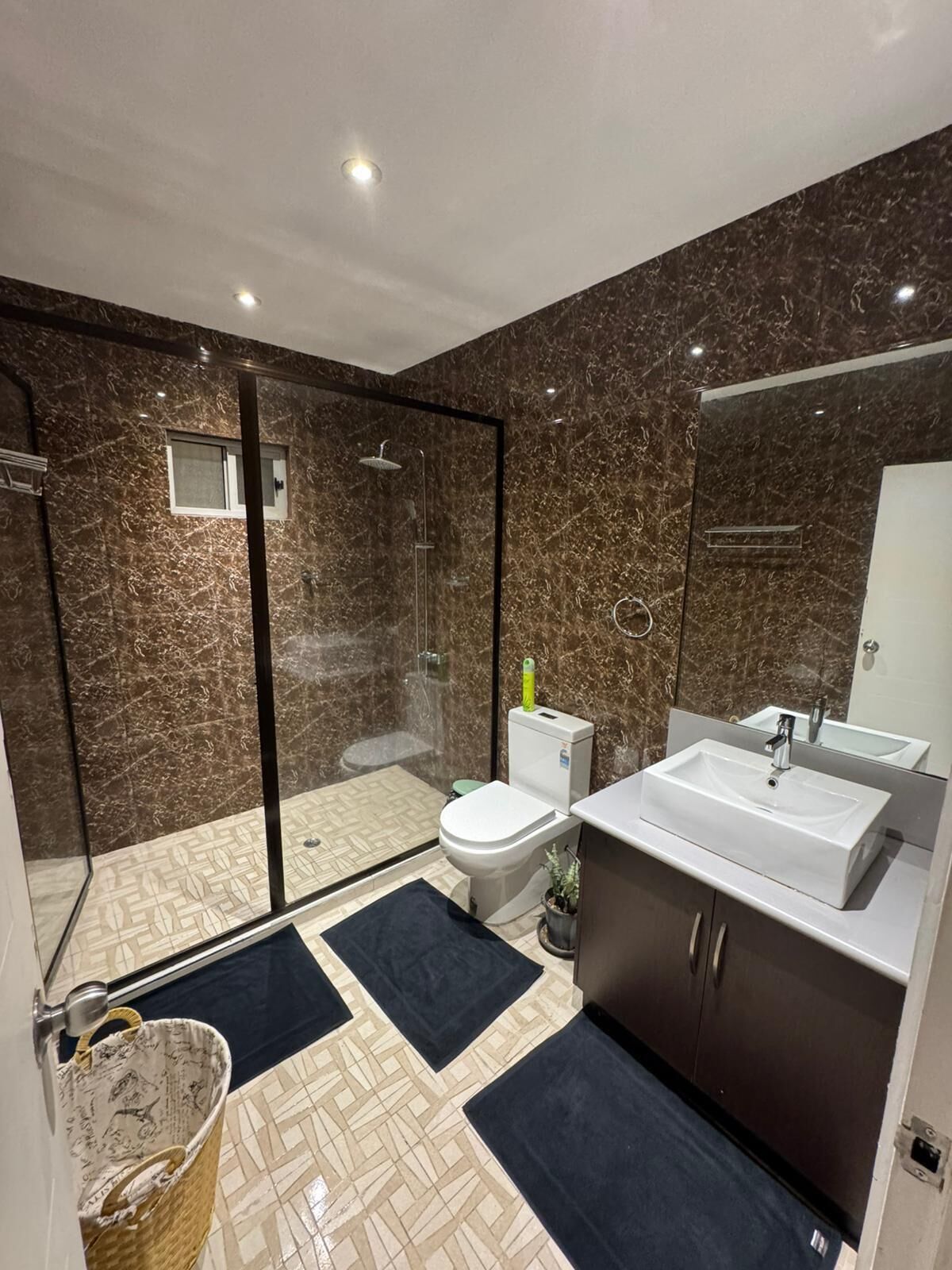 Uma casa de banho moderna com chuveiro de vidro, sanita, lavatório e espelho.