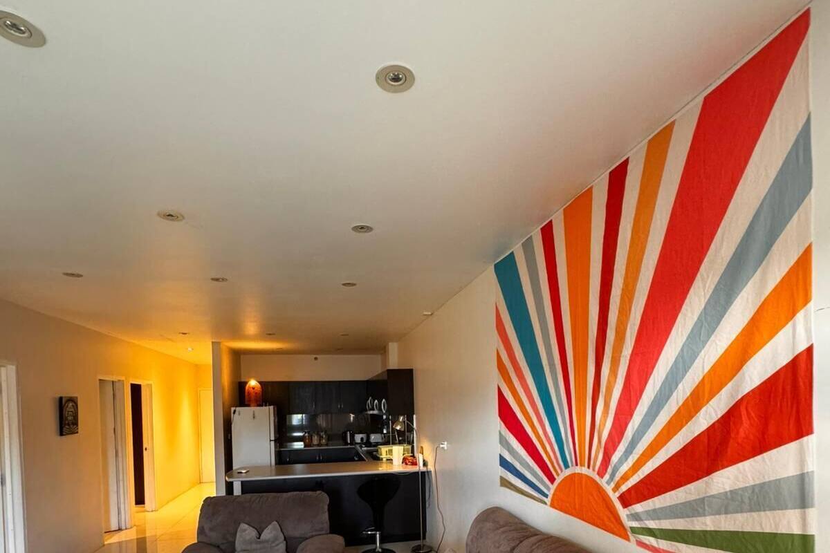 A modern living room with a sofa, a patterned rug, and a vibrant sun mural on the wall.
