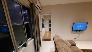 A modern living room with a sofa, a TV mounted on the wall, and a window with curtains. - Bula Bliss (Nadi)