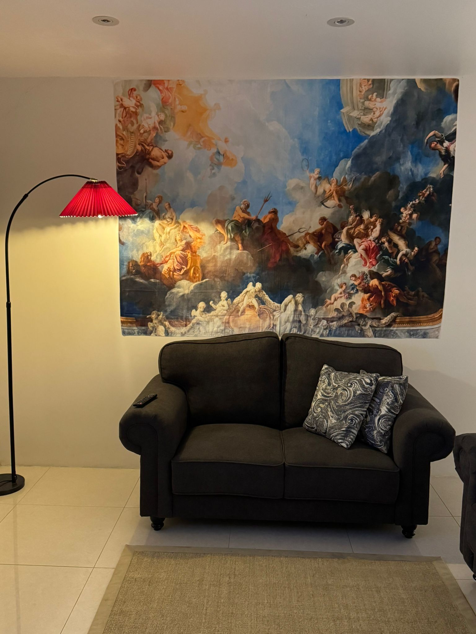 A living room with a large classical painting on the wall, a black sofa, and a red floor lamp.