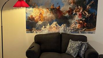 A living room with a large classical painting on the wall, a black sofa, and a red floor lamp.