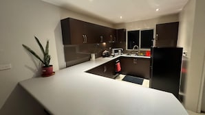 A modern kitchen with dark cabinets, a white countertop, and a black refrigerator. - Bula Bliss (Nadi)