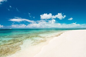 Ein Strand mit klarem, türkisblauem Wasser und weißem Sand unter blauem Himmel mit Wolken.