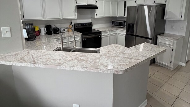A modern kitchen with white cabinetry, a large island with a sink, stainless steel appliances, and a tiled floor. - Comfortable and safe family lodging for everyone close to the medical center.  (Houston)