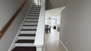 A staircase with dark steps and white handrails, leading to a dining area with a high ceiling and a ceiling fan. - Comfortable and safe family lodging for everyone close to the medical center.  (Houston)