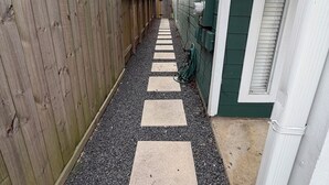 A narrow pathway with stepping stones leading to a building with a green exterior and a wooden fence on one side. - Comfortable and safe family lodging for everyone close to the medical center.  (Houston)