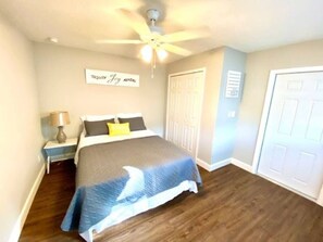 A bedroom with a bed, a nightstand, a lamp, a ceiling fan, and two doors.