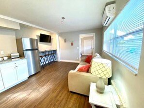 A compact living space with a kitchenette, a sofa, and a TV mounted on the wall.