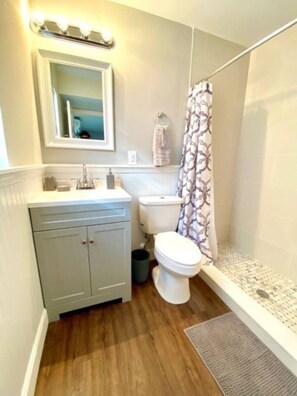 Un baño con suelo de madera, un lavabo blanco, un inodoro y una cortina de ducha.