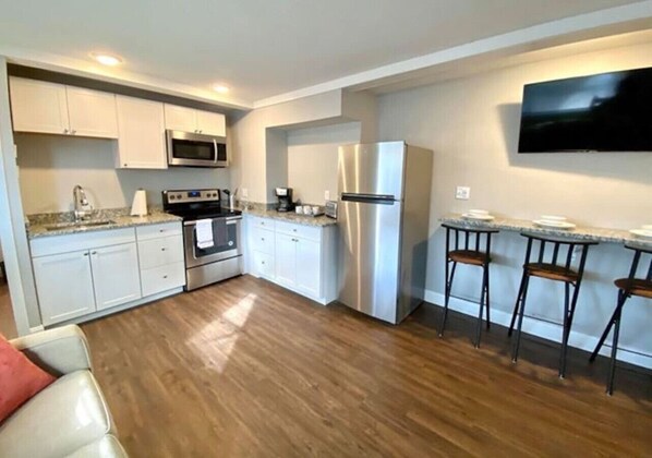 A compact kitchen with white cabinets, stainless steel appliances, and a wooden floor.