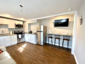 A modern kitchen with white cabinets, stainless steel appliances, and a bar area with stools.