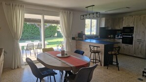 A modern kitchen with a central island, a dining area with a table and chairs, and a view of a garden through large sliding doors.