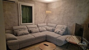 A living room with a large L-shaped sectional sofa, a small round coffee table, a floor lamp, and a television on a stand.