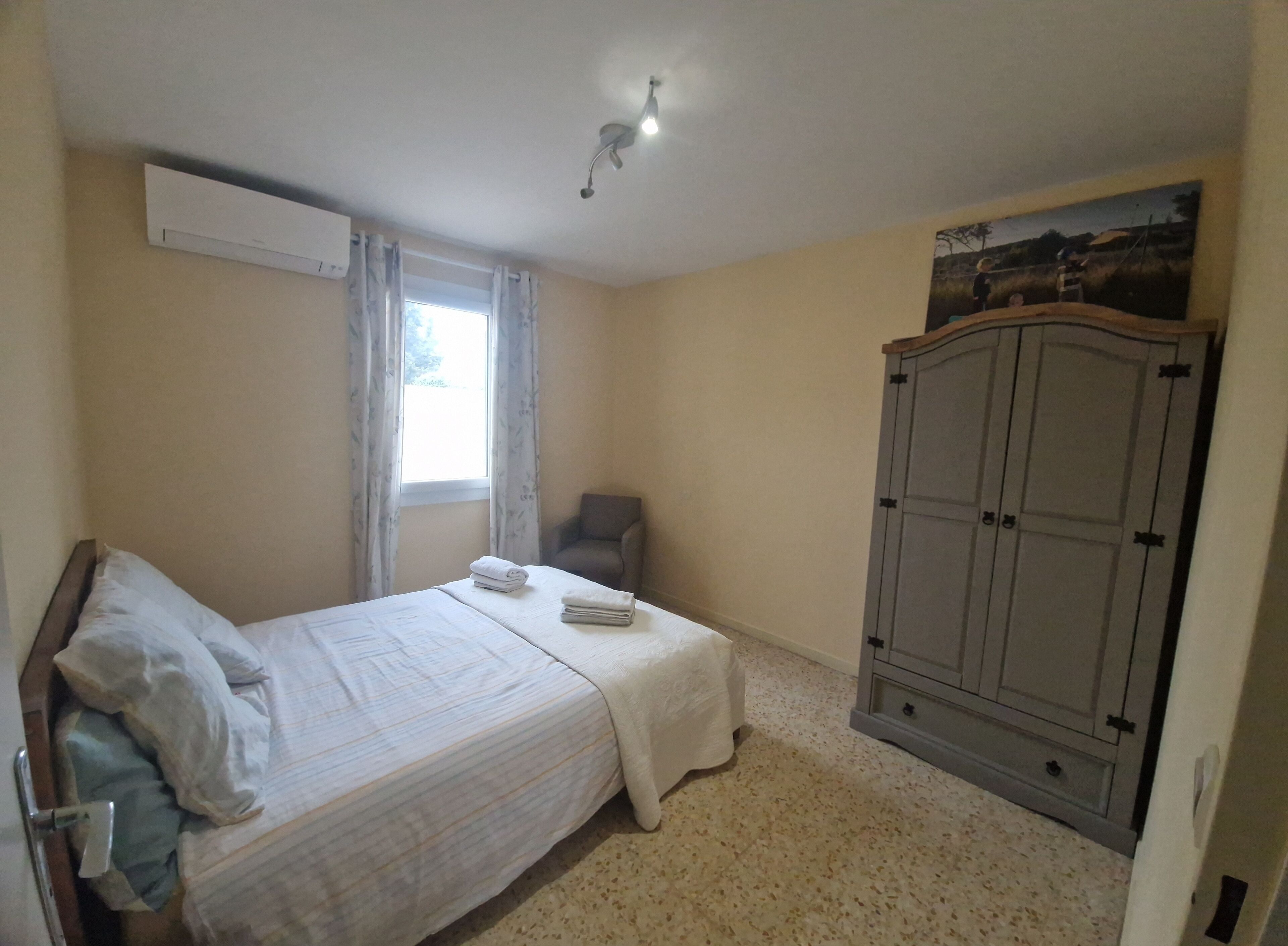 Een slaapkamer met een bed, een stoel, een kledingkast en een raam met gordijnen.
