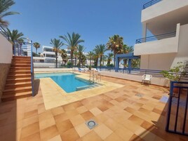 A swimming pool with a blue water feature, surrounded by palm trees and a modern building with balconies.