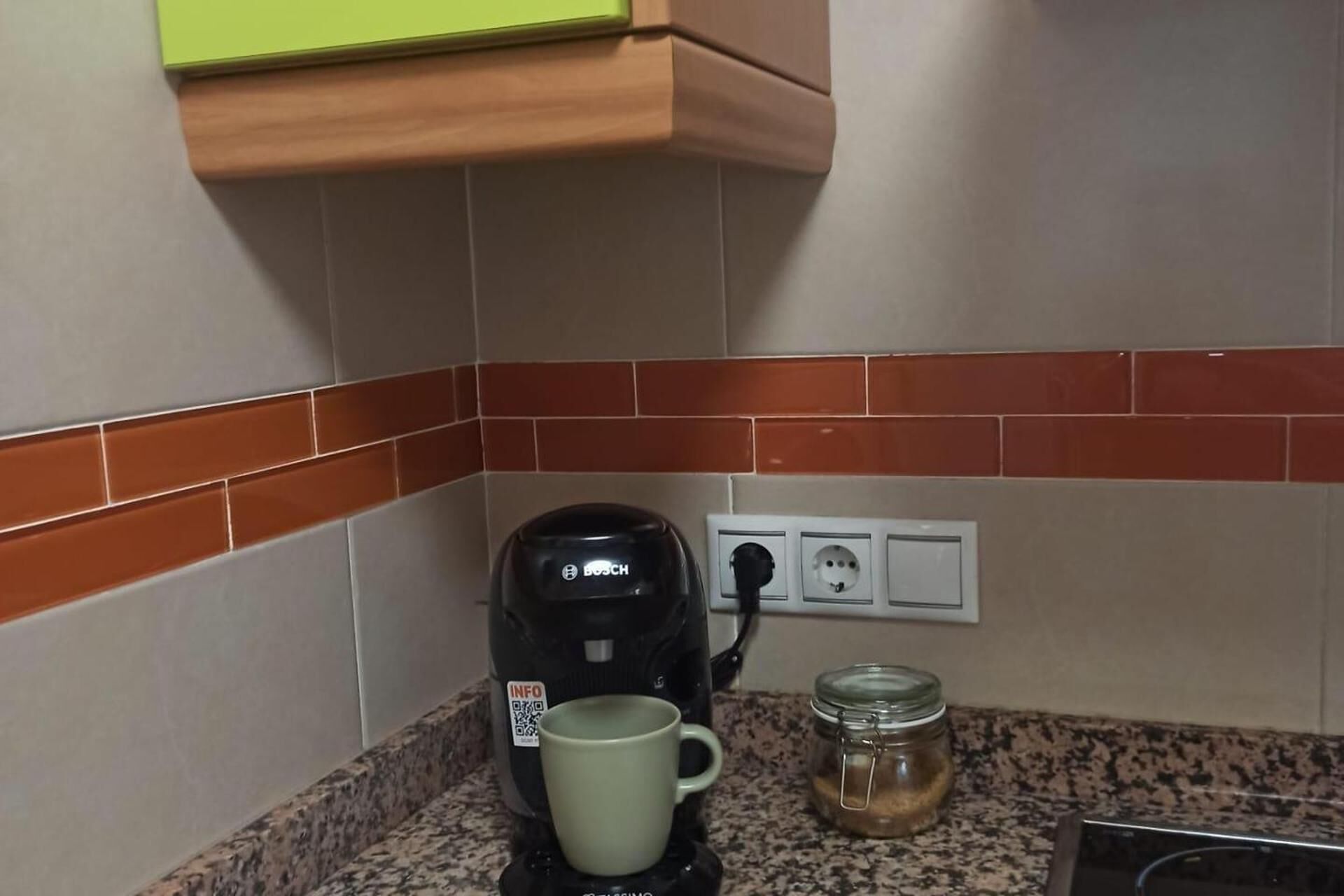 Una cocina con una cafetera, una taza y un tarro sobre la encimera.