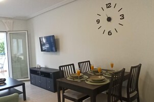 Ein Essbereich mit Wanduhr, Flachbildfernseher und einem Esstisch für vier Personen.