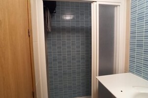 A bathroom with a tiled shower, a wooden door, and a white sink.
