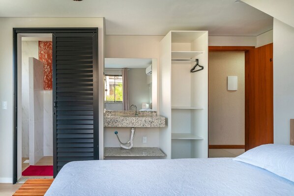 A modern hotel room with a bed, a bathroom with a sink and mirror, and a wardrobe.