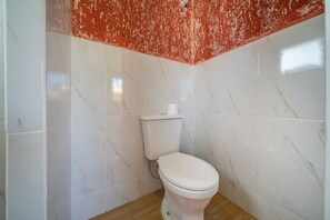 Een badkamer met een toilet, witte marmeren tegels en een rood plafond.