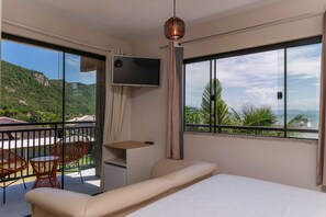 Une chambre avec un lit, une télévision, un balcon avec des chaises et une vue sur un paysage montagneux.
