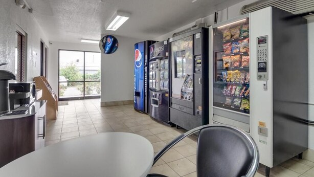 A clean, modern room with a white table, a black chair, and vending machines including Pepsi. - AVERA SUITES (Muskogee)