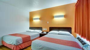 A hotel room with two beds, a wooden floor, a wall-mounted air conditioner, and a window with orange curtains. - AVERA SUITES (Muskogee)