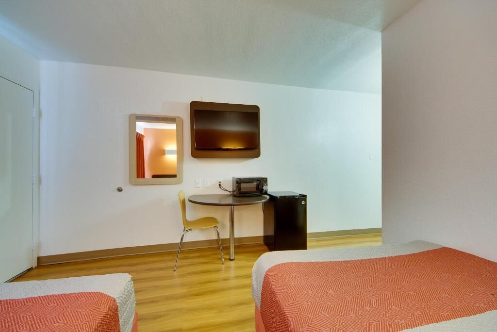 A hotel room with two beds, a small table with a chair, a microwave, and a trash bin.