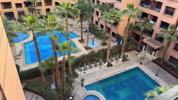 Ein mehrstöckiges Hotel mit Innenhof, der einen Pool, Palmen und Außenbereiche mit Sitzgelegenheiten bietet.