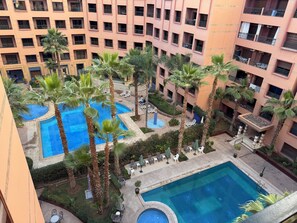 A multi-story hotel with a central courtyard featuring a swimming pool, palm trees, and outdoor seating areas.
