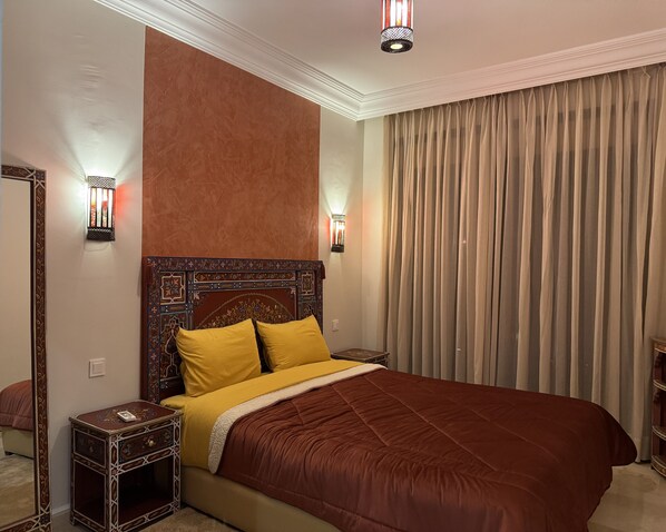 A hotel room with a large bed, two bedside tables, a decorative headboard, and a large window with curtains.