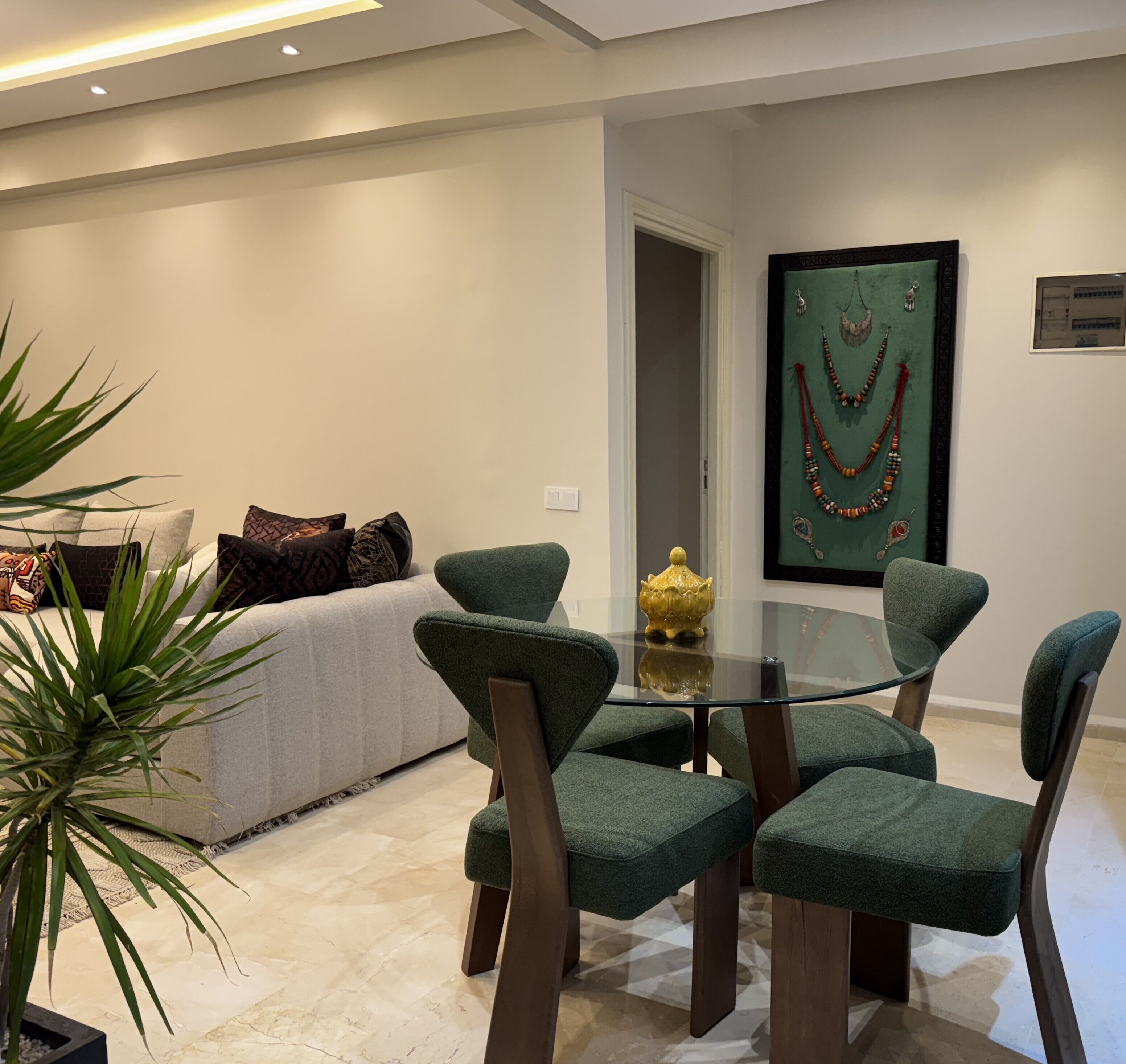 A modern living room with a sofa, green upholstered chairs, a glass coffee table, and a decorative wall piece.