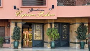 Das  äußere Erscheinungsbild des Caprice Palace mit einem markanten Eingang, großen Kübelpflanzen und einem gefliesten Eingangsbereich.