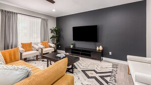 A modern living room with a flat-screen TV mounted on a dark wall, a ceiling fan, and a fireplace. - 3BR Southwest Modern Haven - Old Town (Scottsdale)