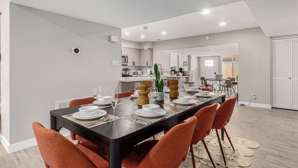A modern dining area with a long table, orange chairs, and a kitchen in the background. - 3BR Southwest Modern Haven - Old Town (Scottsdale)