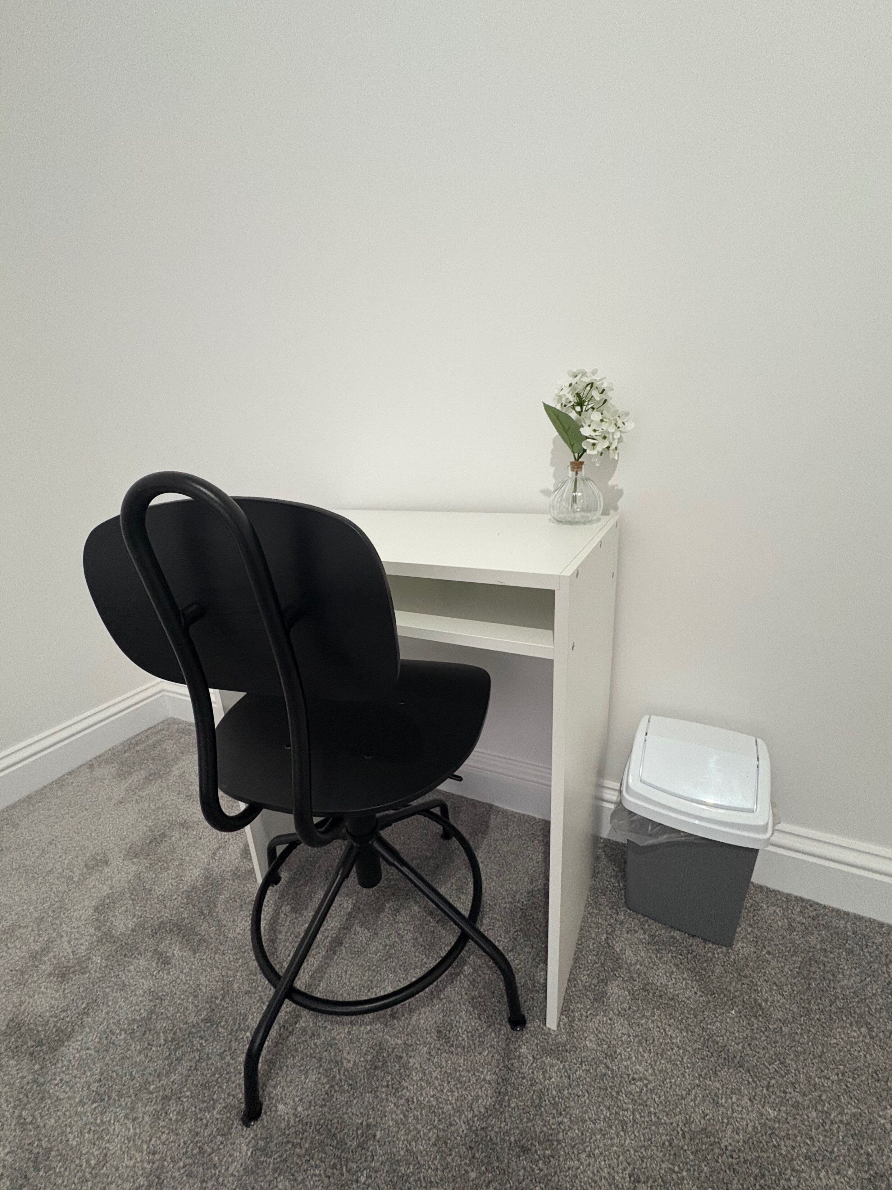 A black office chair with a white desk and a small vase with white flowers.