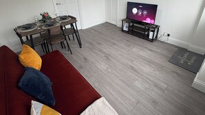 A living room with a red sofa, a wooden dining table set for four, a TV on a stand, and a welcome mat. - Central Chelmsford 2-bed Apt, 5 Mins to Station (Chelmsford)